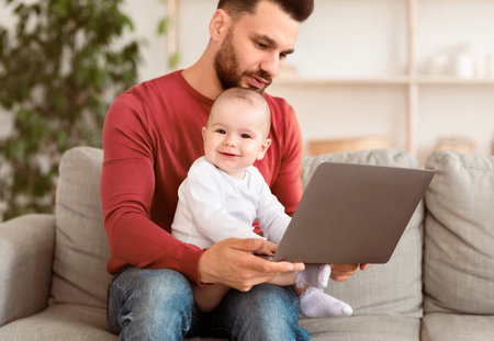 Dad With Baby Working On Laptop Sitting On Couch Indoorの写真素材