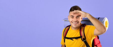 Happy millennial tourist with camping equipment and map looking at camera on blue studio backgroundの写真素材