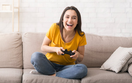 Fun stay home pastimes. Excited Hispanic girl with controller playing video games on sofa indoors