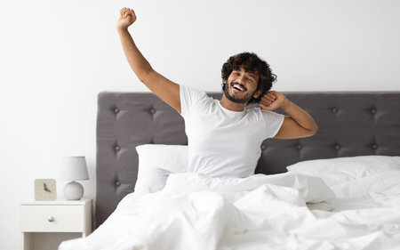 Well-rested guy in pajamas stretching in bed