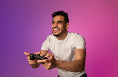 Happy young Arab guy with joystick playing video game in neon light. Modern hobbies conceptの写真素材