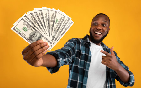 Happy Black Man Holding Money Cash Standing Over Yellow Backgroundの写真素材