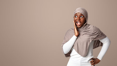 Shocking Offer. Surprised black islamic lady in hijab touching face in excitementの写真素材