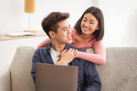 Asian Couple Using Laptop Browsing Internet Sitting In Living Roomの写真素材