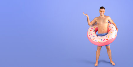 Handsome young guy in swimwear with inflatable ring on blue studio background, copy space