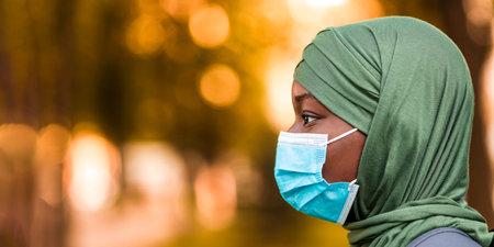 Profile of black muslim woman wearing medical mask and hijab standing outdoorsの写真素材
