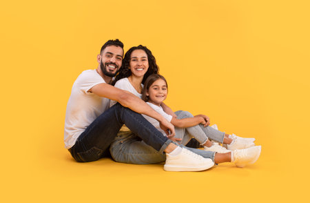Arabic Father, Mother And Daughter Hugging Sitting Over Yellow Backgroundの写真素材