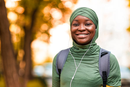 Joyful african islamic woman listening music outdoors with smartphone and earphonesの写真素材