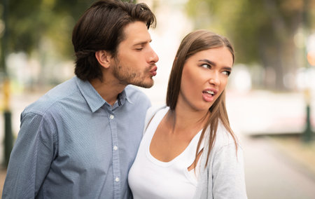 Disgusted Woman Rejecting To Kiss Man Walking Outdoors In Park