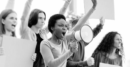 Multiethnic demonstrators protesting on the street, holding megaphone and placardsの写真素材