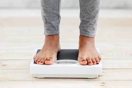 Closeup of young African American woman standing on scales indoors, checking her weight, cropped view of feetの写真素材