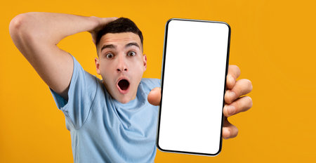 Shocked man showing white empty smartphone screen close to cameraの写真素材
