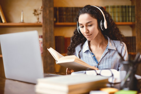Lady sitting at desk, wearing headset, using computer, reading bookの写真素材