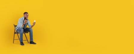 Man sitting on chair laughing while using smartphone in bright settingの写真素材