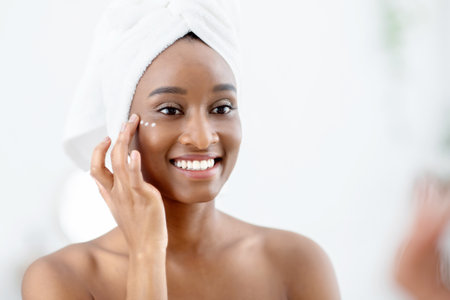 Cheerful young female blogger demonstrating organic cream, applying on face after shower in morningの写真素材
