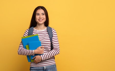 Cheerful student holding colorful notebooks against a bright yellow backgroundの写真素材