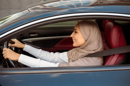 Cheerful happy muslim woman in hijab driving her new car