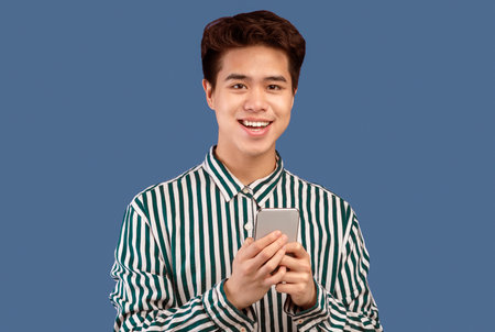 Smiling young asian man using mobile phone at studio