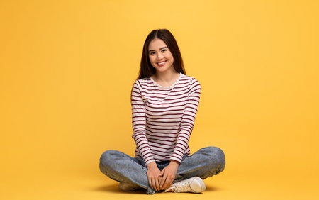 Young woman in casual wear sitting cross-legged on yellow backgroundの写真素材