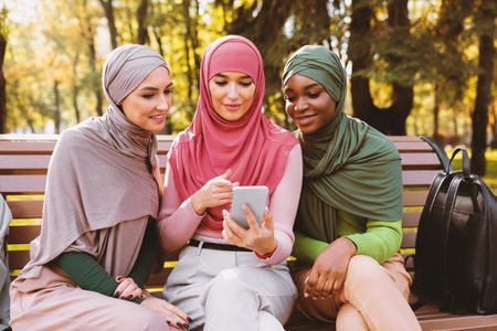 Muslim Students Ladies Using Smartphone With Educational App Sitting Outdoorの写真素材