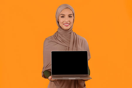 Muslim Woman Showing Blank Laptop Screen Over Yellow Studio Backgroundの写真素材