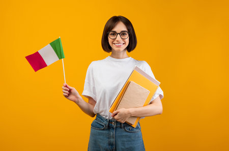 Learning Italian, student exchange and travel. Happy lady holding notebooks and small flag of Italy, orange backgroundの写真素材