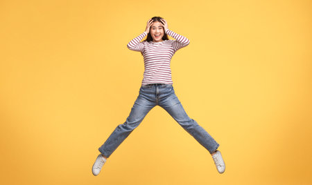 Joyful young woman jumping against a bright yellow background in casual attire