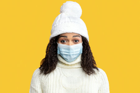 Portrait of black lady in medical mask and winter hatの写真素材