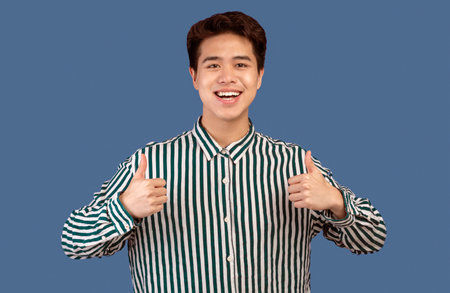 Happy asian guy gesturing thumbs up and smiling