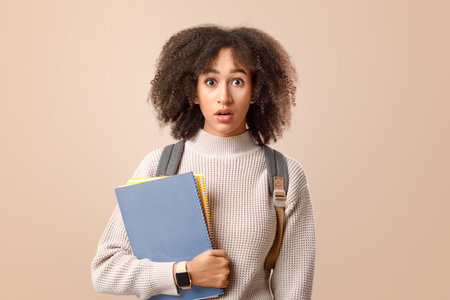 Surprised african american woman with open mouth with backpack and smart watch holding notepadsの写真素材