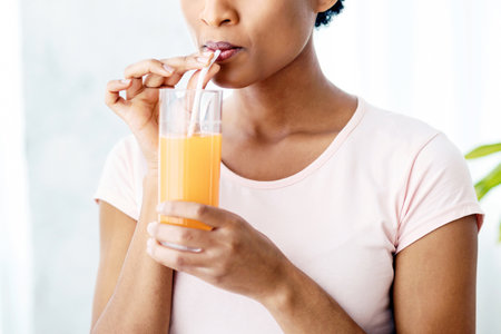 Pretty black woman drinking fresh orange juice at home, panoramaの写真素材