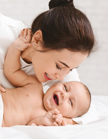 Mother tickling her baby playing in bed at home