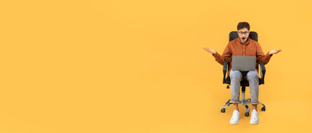 Surprised young man sitting in office chair while using laptopの写真素材