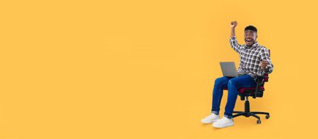 Young man celebrates success at a desk in a bright yellow roomの写真素材