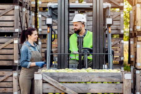 Happy young bearded guy driver in helmet in forklift truck with box full green applesの写真素材