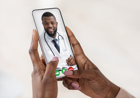 Handsome black doctor consulting female patient remotely by video call on smartphone