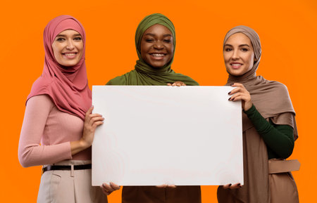 Three Muslim Women Holding Empty Poster Standing Over Yellow Backgroundの写真素材