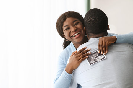 Excited black woman holding ultrasound image and hugging her manの写真素材