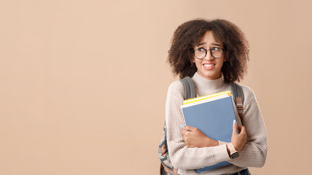 Sad african american lady in glasses with backpack and smart watch holds notepadsの写真素材