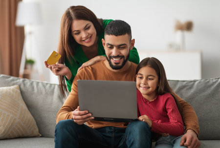 Arabic family using laptop computer and credit card at homeの写真素材