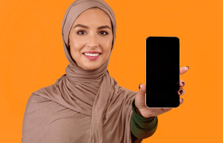 Muslim Woman Showing Smartphone Blank Screen Standing Over Yellow Background
