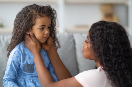 Family misunderstanding, childhood problems. Young black mother comforting her sad offended daughter at homeの写真素材