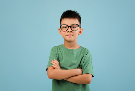 Portrait of smiling little asian boy wearing eyeglasses standing with folded arms