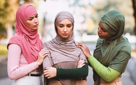 Three Muslim Women Comforting Supporting Unhappy Female Friend Standing Outdoorsの写真素材