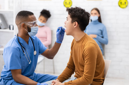 African Doctor Testing Asian Patient For Coronavirus Sitting In Clinicの写真素材