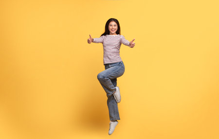 Young woman joyfully jumping against a bright yellow backgroundの写真素材