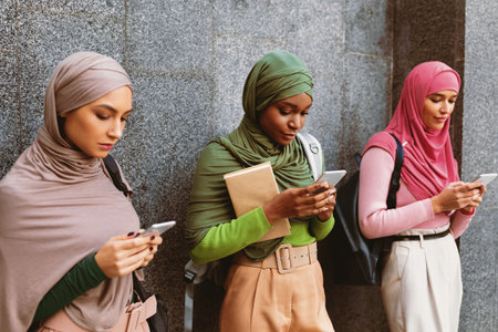Diverse Islamic Ladies Using Phones Standing Over Gray Wall Outdoorの写真素材
