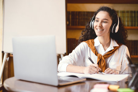 Lady sitting at table, using laptop and writing in notebook
