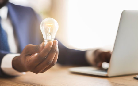 Businessman holding illuminated light bulb, sitting in officeの写真素材