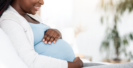 Black Pregnant Woman Sitting On Bed At Embracing Belly, Side View
